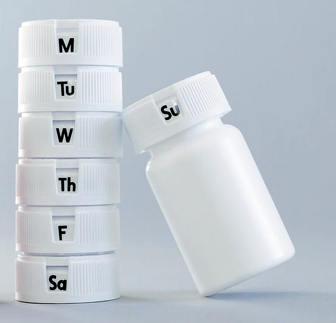 A stack of RedCap closures marked M, Tu, W, Th, F, Sa beside a capped prescription bottle.
